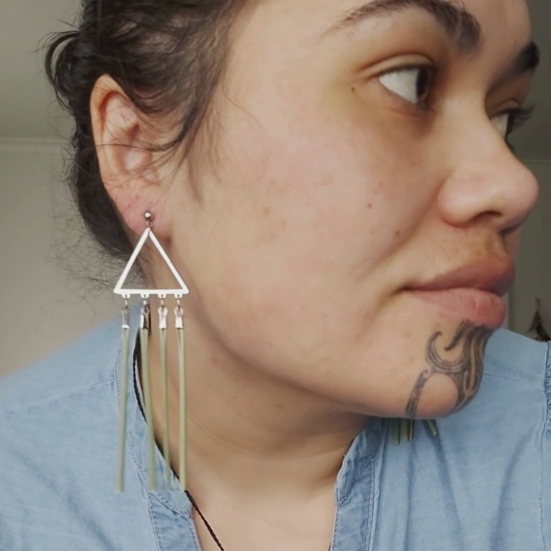 KIHI TOI Tīaho earrings close up video. Stainless steel ear studs, stainless steel triangle chandelier, Four strands of wharariki nz flax. Flax strands approxiamtely 6.5cm in length